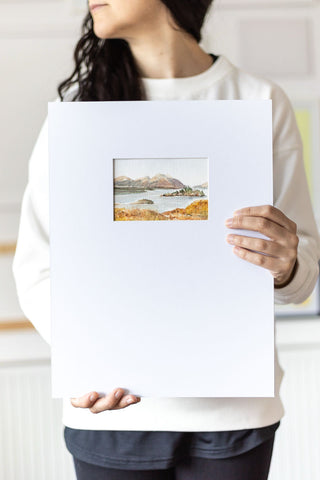 woman holding a landscape watercolor painting on a large mat