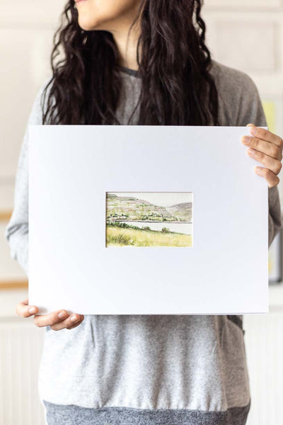 woman holding a landscape watercolor painting on a large mat
