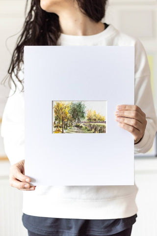 woman holding a landscape watercolor painting on a large mat