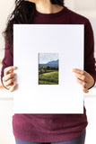 woman holding a landscape acrylic painting on a large mat