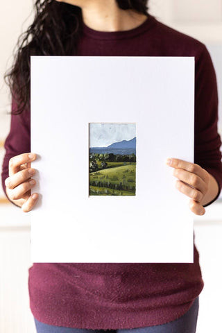 woman holding a landscape acrylic painting on a large mat