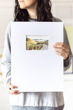 woman holding a landscape watercolor painting on a large mat