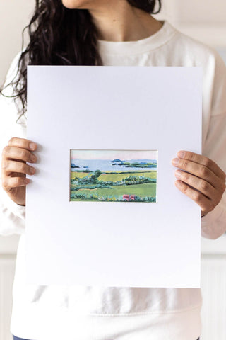 woman holding a landscape acrylic painting on a large mat