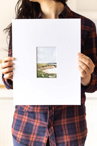 woman holding a landscape watercolor painting on a large mat