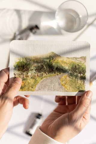 hands holding a loose watercolor landscape painting