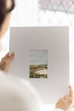 woman holding a landscape acrylic painting on a large mat