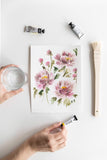 pink watercolor flowers painting on a table next to tube paints and brush