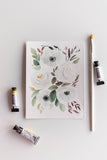white watercolor flowers bouquet next to brush and paint tubes Flavia Bennard