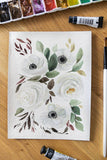 white watercolor flowers bouquet next to brush and paint tubes Flavia Bennard